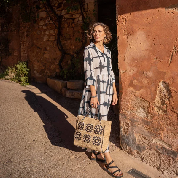 Photo posée d'une femme en tunique noire et blanche avec un sac en raphia beige noir