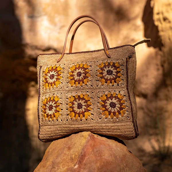 Photo sur des rochers, un sac en raphia beige et lanières de cuir à motifs colorées