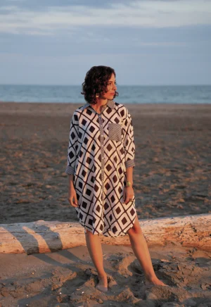 photo posée une femme tunique blanche à motifs noir sur le sable au bord de l'eau