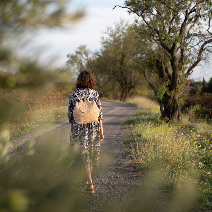 une femme avec un sac à dos beige en raphia Bagatelle France